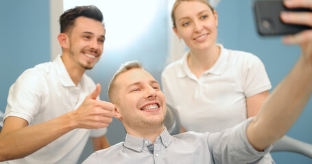 Young male patient in dental braces making selfie photo with a dentist and assistant during a regular orthodontic visit at the dental office. 4k video screenshot, please use in small size
