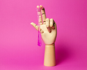 Wooden hand with dripping pink liquid paste pink background. Hair removal and sex concept.