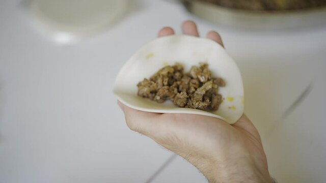 Close up of male hands preparing an argentinean empanada over a white table. Putting the filling and closing it with a home made traditional repulgue.