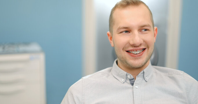 Portrait of a young male patient wearing dental braces smiling at camera, sitting on a dental chair during an orthodontic visit. 4k video screenshot, please use in small size