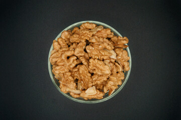 walnuts in a glass round bowl on a black background as a source of vitamins