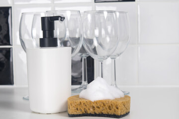 glass glasses on a stem and a bottle of cleaning agent next to a sponge with a thick foam