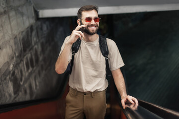 Happy young man talk on smartphones while standing on escalator. Modern people with cell phones outdoor. Mobile communication technology. High angle view