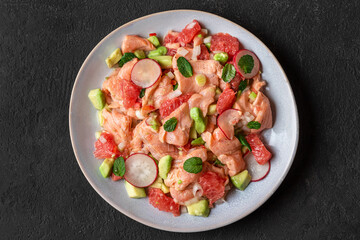 Salmon ceviche with grapefruit, avocado, radish, onion and mint in a plate on dark background. Healthy diet food. top view