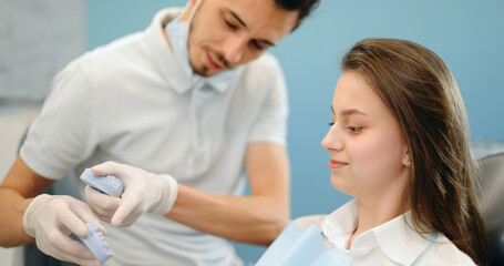 Dentist showing a jaw model, explaining to the young patient the process of orthodontic treatment. Girl with dental braces with a dentist. 4k video screenshot, please use in small size