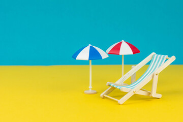 Fototapeta na wymiar Beach relaxation and vacation concept. Toy sun lounger and umbrella on colorful paper background. 