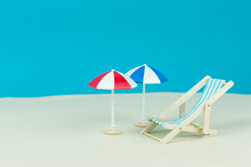 Beach relaxation and vacation concept. Toy sun lounger and umbrella on sand and colorful paper background.
