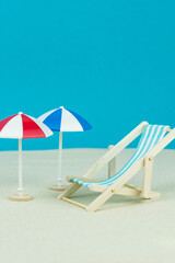 Beach relaxation and vacation concept. Toy sun lounger and umbrella on sand and colorful paper background.