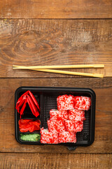 Roll with shrimp, cucumber, cream cheese and tobiko caviar and sticks in a box and soy sauce in a sauce bowl with ginger on a wooden background. copy space