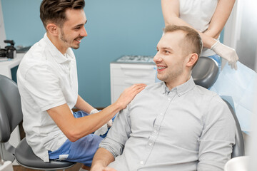 Obraz premium Small talk between patient and dentist , preparing for the dental check up at the dental office. Regular visit to the orthodontist. Patient smiling and looking at the doctor. High quality photo
