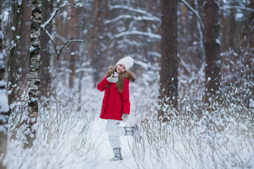 Beautiful little girl wearing red jacket and knitted hat playing in a snowy winter park. Child playing with snow in winter. Kid play and jump in snowy forest.