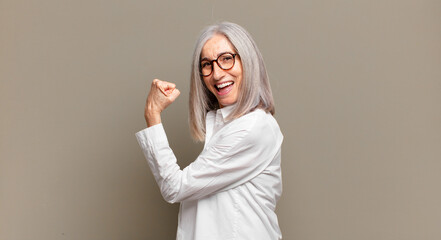 senior woman feeling happy, satisfied and powerful, flexing fit and muscular biceps, looking strong...
