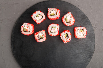 Roll with shrimp and tobiko caviar on a black round board on a gray background.