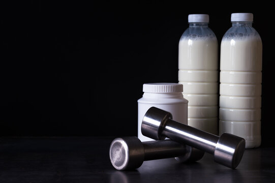 Dumbbells with protein powder and milkshake bottles in plastic packaging on a dark metal background. Background.