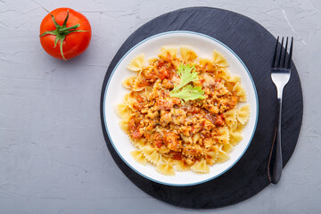 Pasta in tomato bolognese sauce on a black stand on a concrete background near a fork and ripe tomato