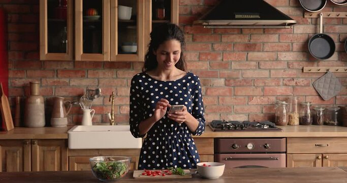 Woman stand in kitchen prepare vegetable salad, use smartphone search vegetarian dish ideas, food recipe on internet, make product delivery order. Modern tech, diet mobile app, healthy eating concept