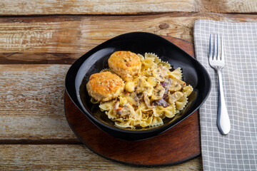 Pasta in a creamy sauce with mushrooms and chicken meatballs in a black plate on a napkin next to a fork.