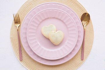 table setting. two empty pink plates, two heart cookies, a spoon and a fork on a white table. copy space.