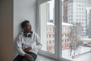 Fototapeta premium young male african american student sitting on a windowsill in an educational institution