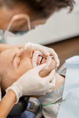 Young male patient with dental braces during a regular orthodontic visit. Dentist adjusting orthodontic brackets, close-up on patient's mouth
