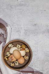 fresh quail and chicken eggs from the farm in a brown clay plate on a gray marble table. selective soft focus. top view .
