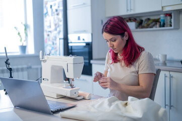 Caucasian woman learning to sew from a video tutorial while sitting in the kitchen. Home hobby for...