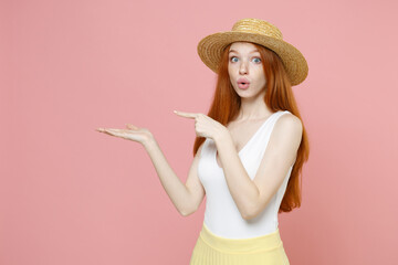Young surprised nice caucasian redhead woman ginger long hair in straw hat summer clothes point...