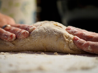 hands of a young woman with a bread dough in a white table