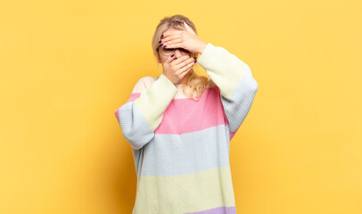 blonde woman covering face with both hands saying no to the camera! refusing pictures or forbidding...