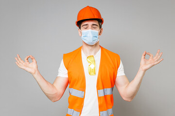 Young employee man in orange vest protective helmet face mask coronavirus covid-19 do yoga gesture meditate isolated on grey background studio Instruments for renovation apartment Repair home concept.