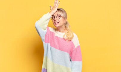 blonde woman raising palm to forehead thinking oops, after making a stupid mistake or remembering,...