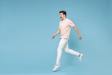 Fototapeta na wymiar Full length side view of young caucasian attractive surprised happy excited student happy man 20s wear beige t-shirt, white pants sneackers running isolated on blue color background studio portrait.