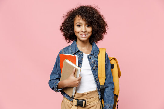 Smiling smart little african american kid school girl 12-13 years old in casual denim clothes with backpack holding books isolated on pastel pink background studio portrait Childhood education concept