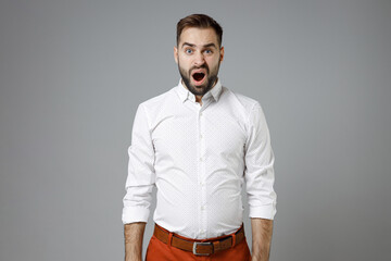 Fototapeta na wymiar Shocked worried young bearded business man wearing classic white shirt standing keeping mouth open looking camera isolated on grey color background studio portrait. Achievement career wealth concept.
