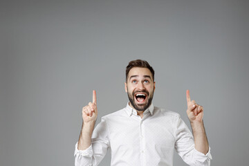 Surprised young bearded business man in classic white shirt standing pointing index fingers up on...