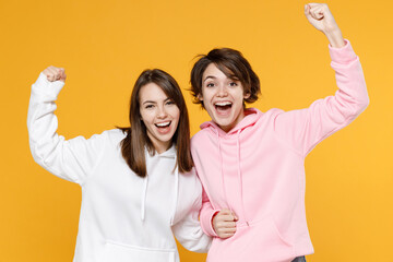 Cheerful happy two young women friends 20s wearing casual white pink hoodies doing winner gesture...