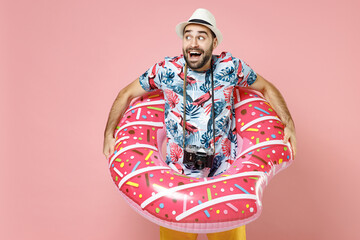 Shocked young traveler tourist man in summer clothes hat photo camera hold inflatable ring isolated on pink background studio portrait. Passenger traveling on weekends. Air flight journey concept.
