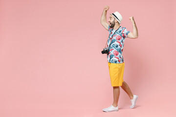 Full length side view of excited traveler tourist man in summer clothes hat doing winner gesture celebrating isolated on pink background. Passenger traveling on weekends. Air flight journey concept.