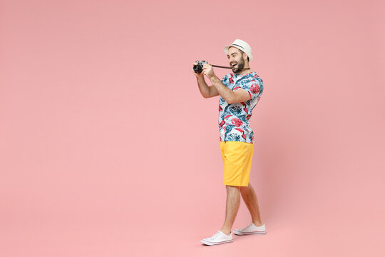 Full length side view of funny traveler tourist man in summer clothes hat taking pictures on vintage photo camera isolated on pink background. Passenger travel on weekends. Air flight journey concept.
