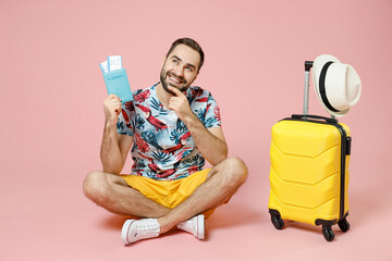 Full length pensive traveler tourist man sit on floor near suitcase hold passport tickets put hand...