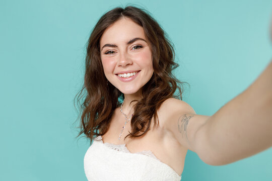 Close Up Of Smiling Bride Young Woman In Beautiful White Wedding Dress Doing Selfie Shot On Mobile Phone Isolated On Blue Turquoise Wall Background Studio Portrait. Ceremony Celebration Party Concept.