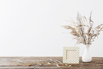 frame and dried flowers in white vase on old wooden shelf