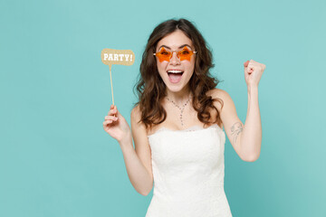 Excited bride young woman 20s in beautiful white wedding dress glasses hold photo props doing winner gesture isolated on blue turquoise background studio portrait. Ceremony celebration party concept.
