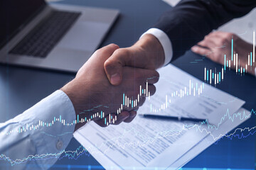 A handshake symbolize a capital market transaction to proceed profitable business in stock trading. Financial hologram chart overt the table with the document.