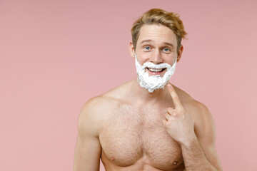 Funny bearded naked young man 20s perfect skin pointing index finger on face covered with shaving...