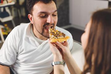 Happy couple at home feeding each other with pizza, dating at home. Care and love concept.