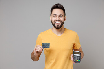 Young caucasian smiling bearded man in casual yellow basic t-shirt hold wireless modern bank...