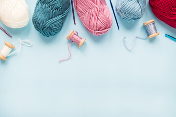 Multicolored crochet hooks with balls of yarn on a blue background with copy space.