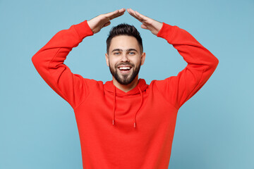 Young caucasian happy bearded optimistic man 20s in casual red orange hoodie Holding folded hands above head like roof, stay home isolated on blue background studio portrait People lifestyle concept