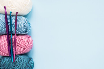 Multicolored crochet hooks with balls of yarn on a blue background with copy space.